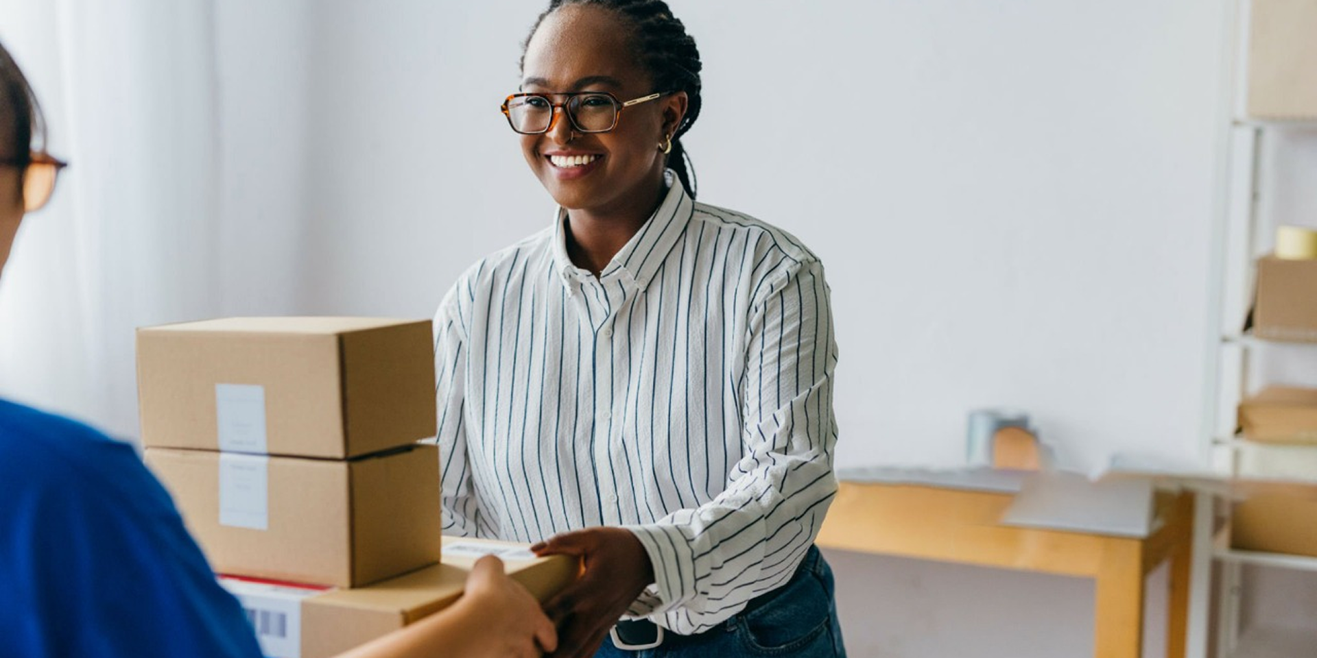 Smiling woman in striped shirt receiving package from delivery person in bright office space